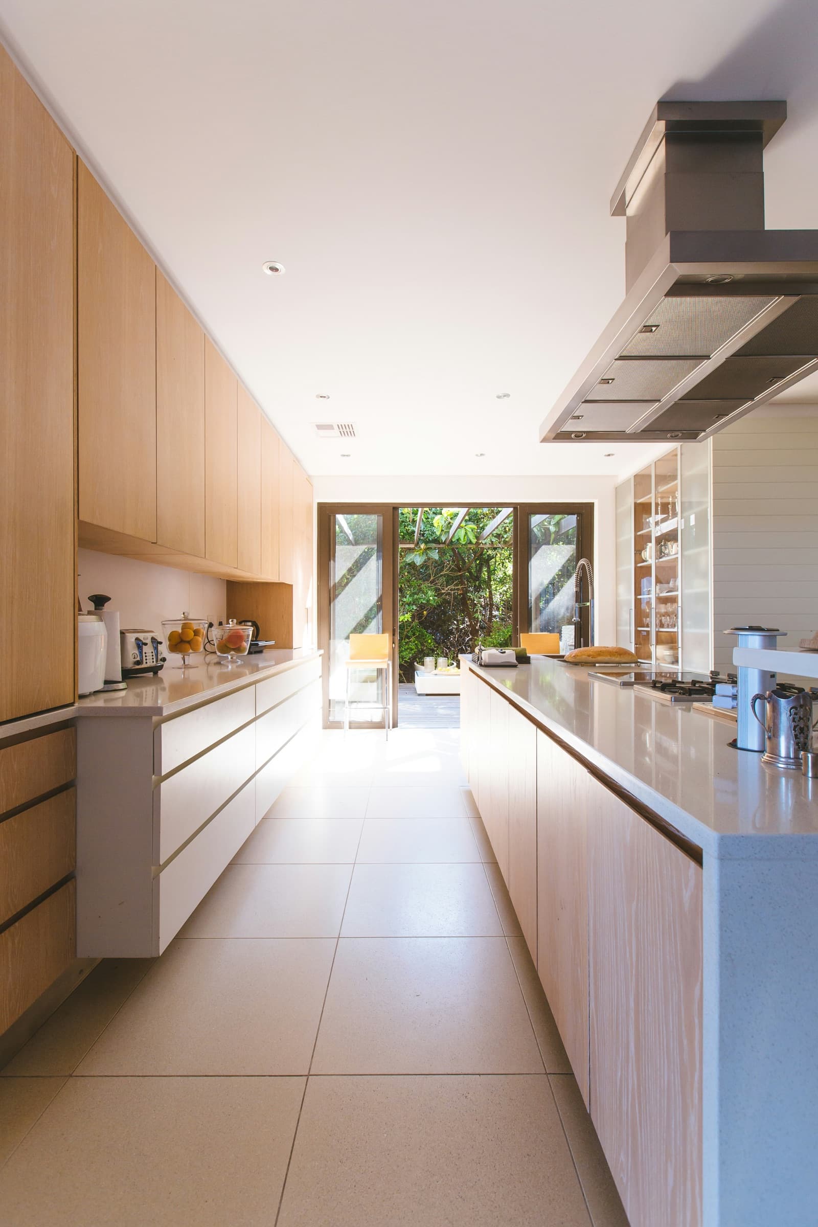 Fitted galley kitchen in pale timber opening onto a garden